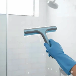 A squeegee removing water from a glass shower door to prevent soap scum and water spots, an indispensable bathroom cleaning utensil.