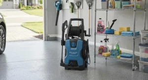 A compact electric pressure washer stored neatly in a suburban garage next to cleaning supplies.
