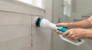 A demonstrative shot of a lightweight, battery-operated scrubber effectively cleaning bathroom tile grout for an elderly user.