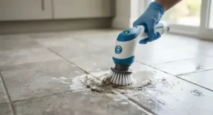 Close-up of an electric spin scrubber effectively removing dirt from kitchen tile grout lines.
