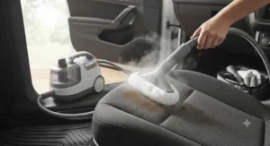 A compact steam cleaner with attachments for upholstery being used to remove stains from car seats.