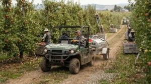 A utility vehicle hauling a pressure washer with water tank for remote areas near an orchard shed.